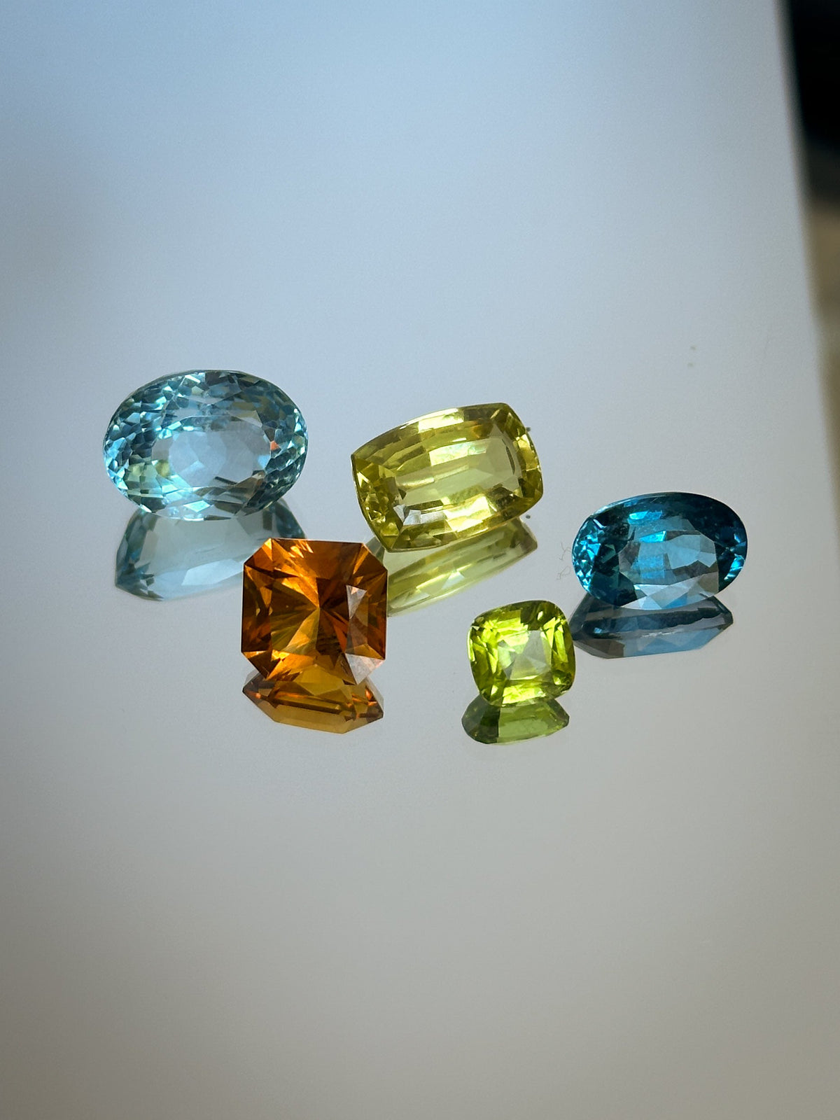 a mix of gemstones on a white background - oval blue topaz, chrysoberyl, citrine, london blue topaz, and peridot