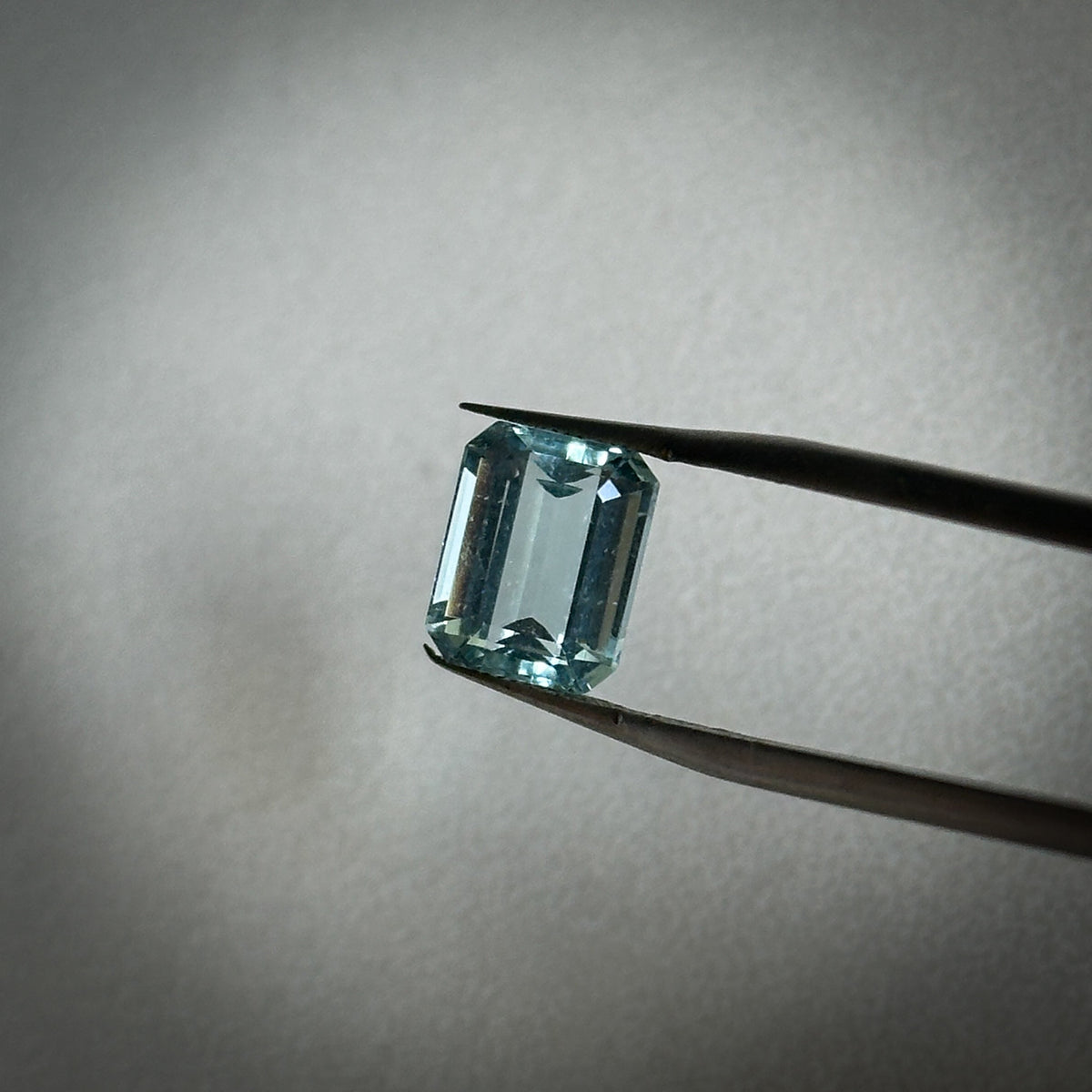 fancy emerald cut medium toned blue aquamarine gemstone held in tweezers 