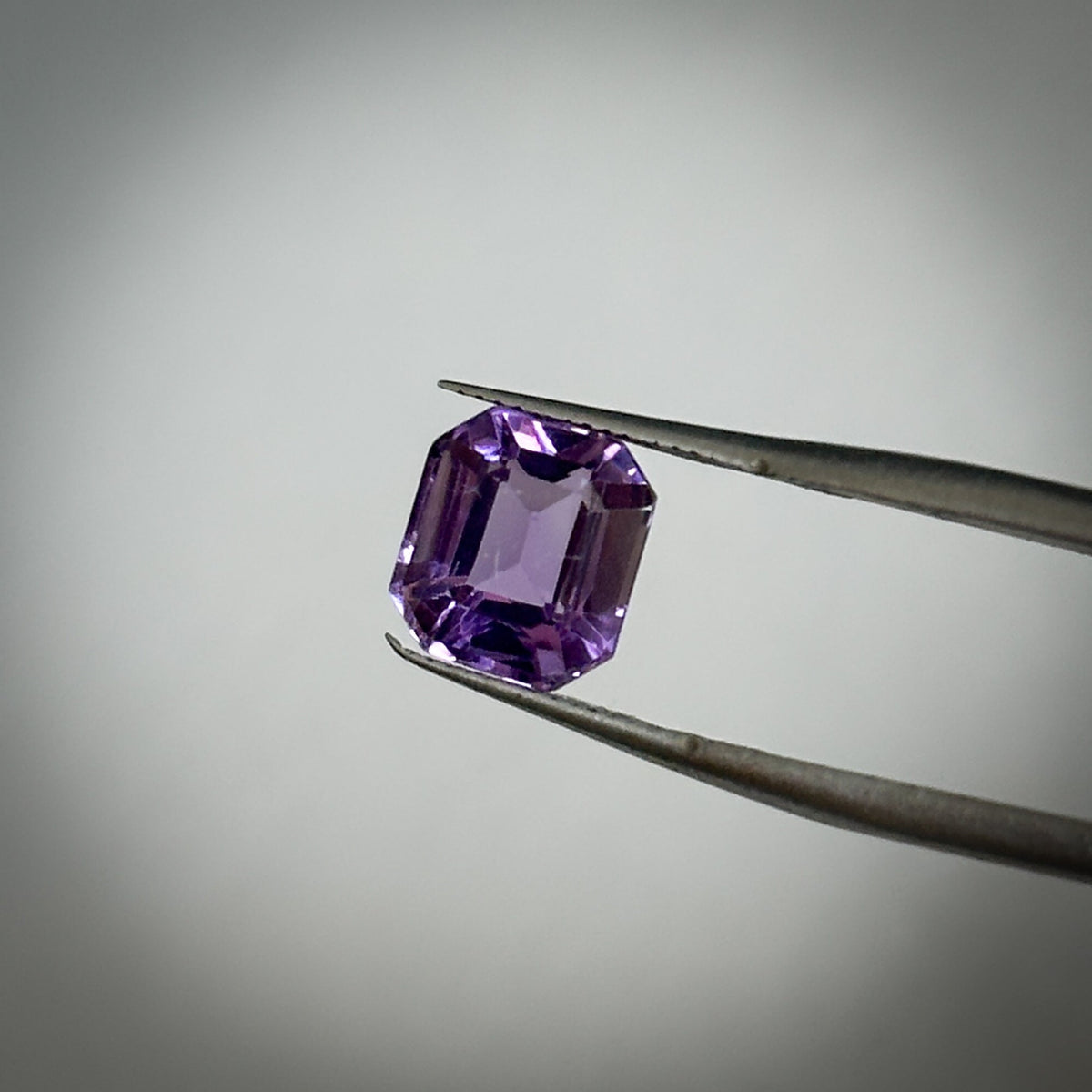emerald cut medium toned purple amethyst gemstone held in tweezers 