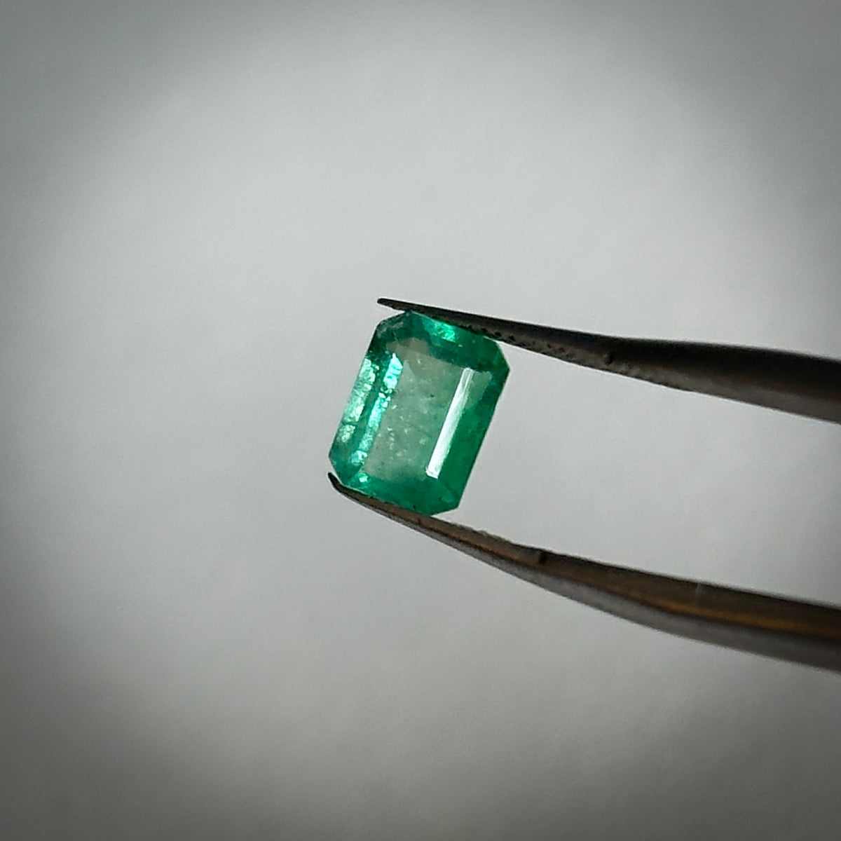 emerald cut medium toned green natural emerald gemstone held in tweezers 