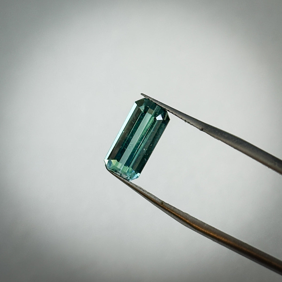 fancy emerald baguette cut medium toned green tourmaline gemstone held in tweezers 