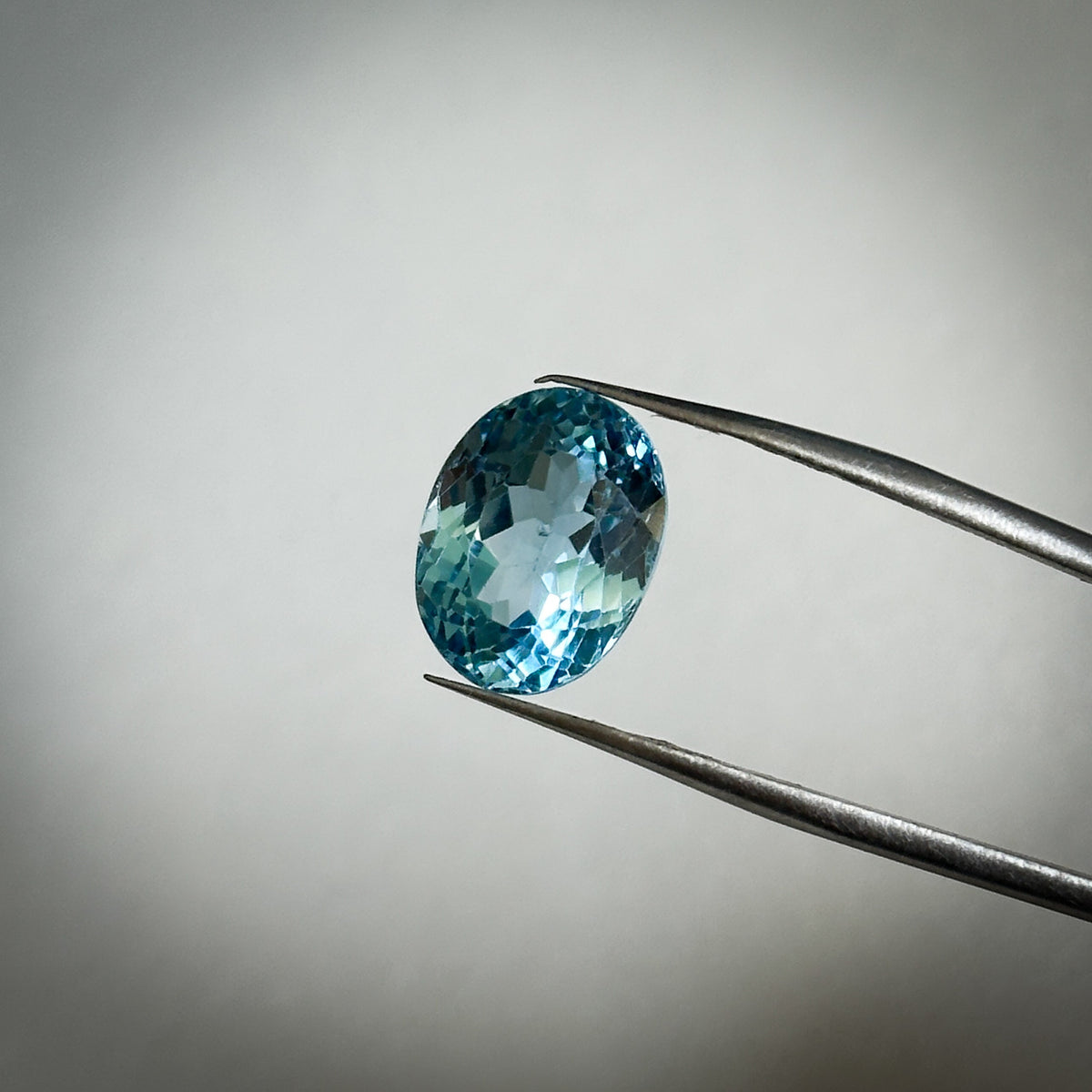 fancy oval cut medium toned blue topaz gemstone held in tweezers 