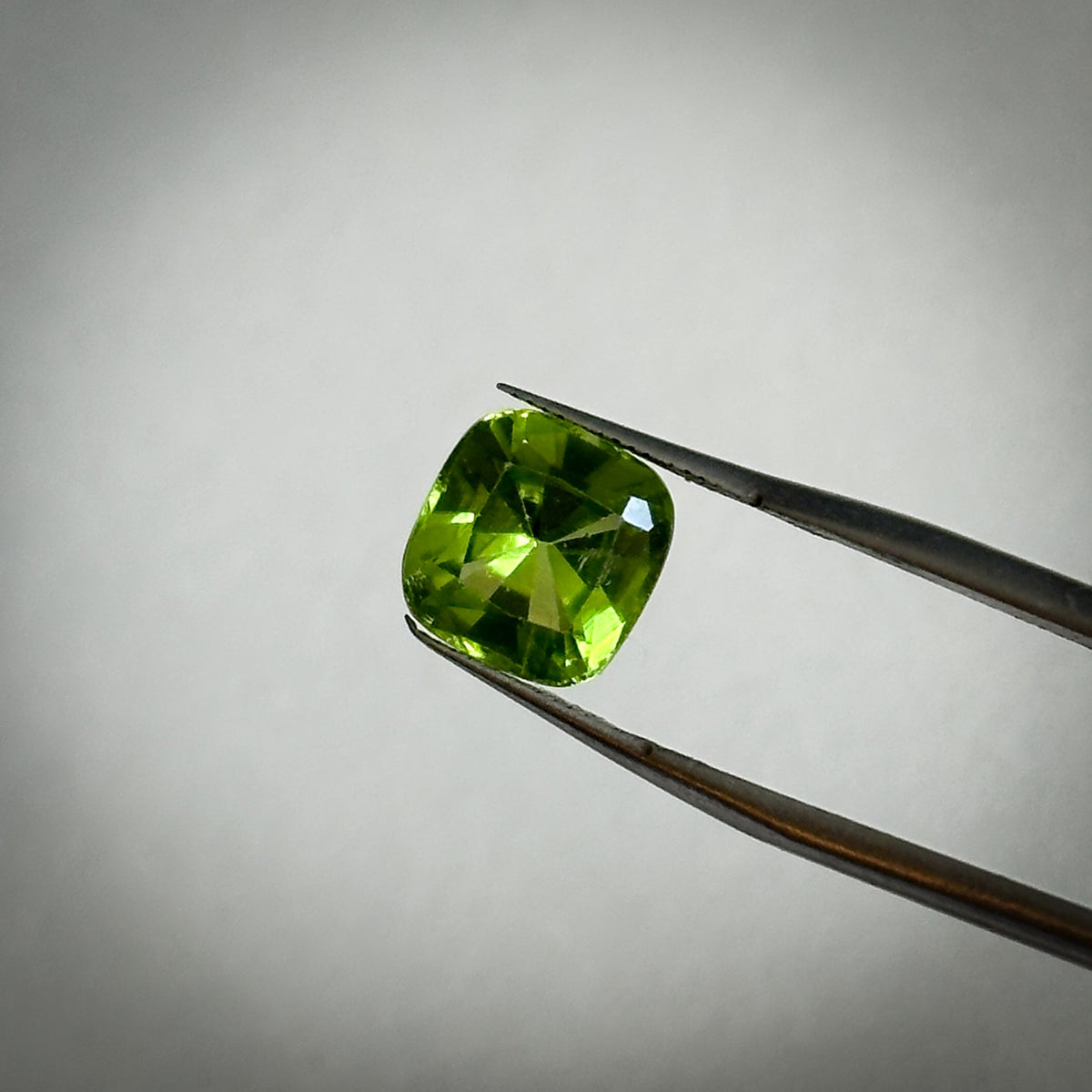 fancy cushion cut medium toned vibrant green peridot gemstone held in tweezers 