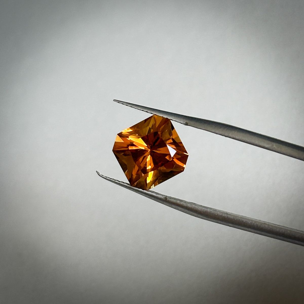 fancy square cut deep orange citrine quartz gemstone held in tweezers 