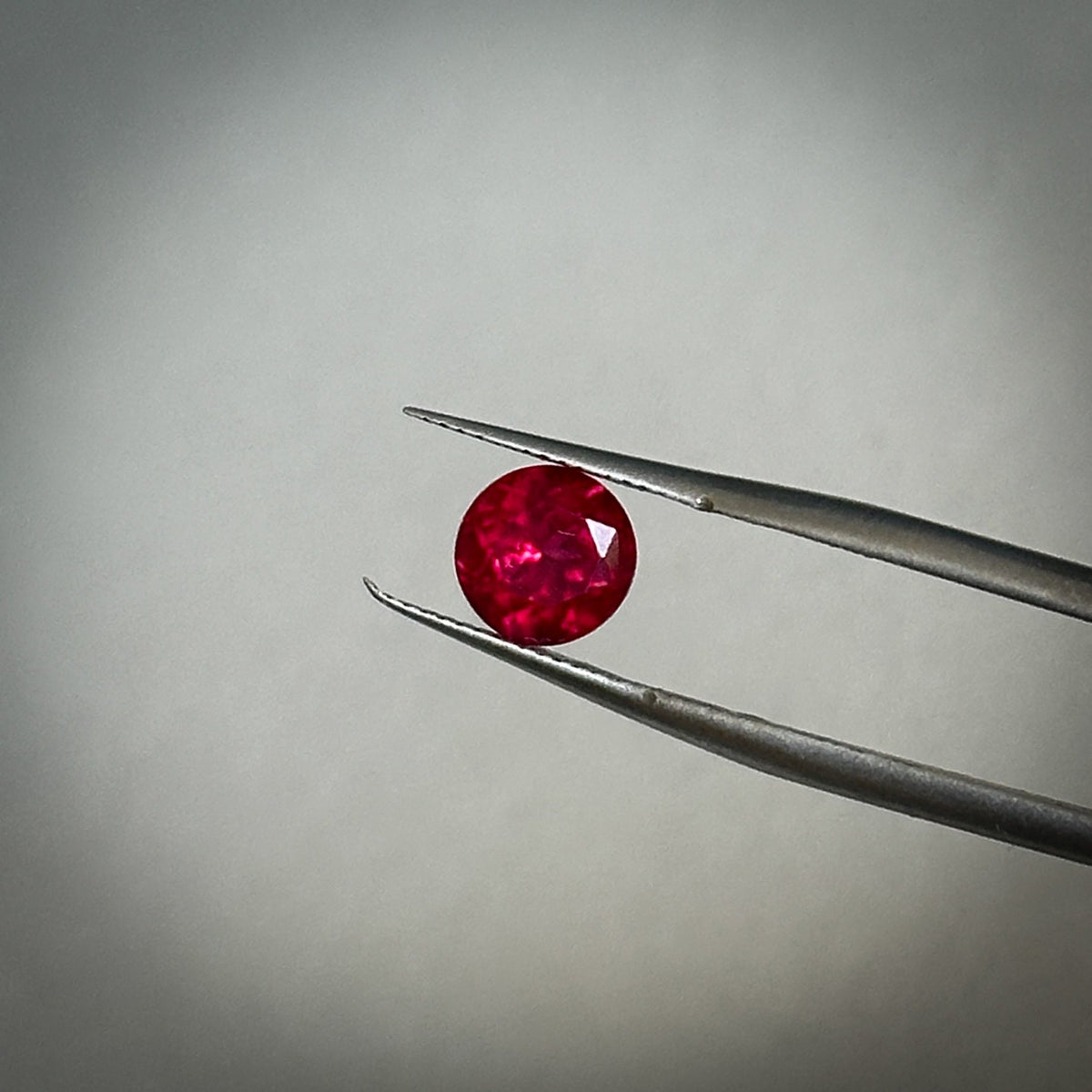 round brilliant cut medium toned vibrant red ruby gemstone held in tweezers 