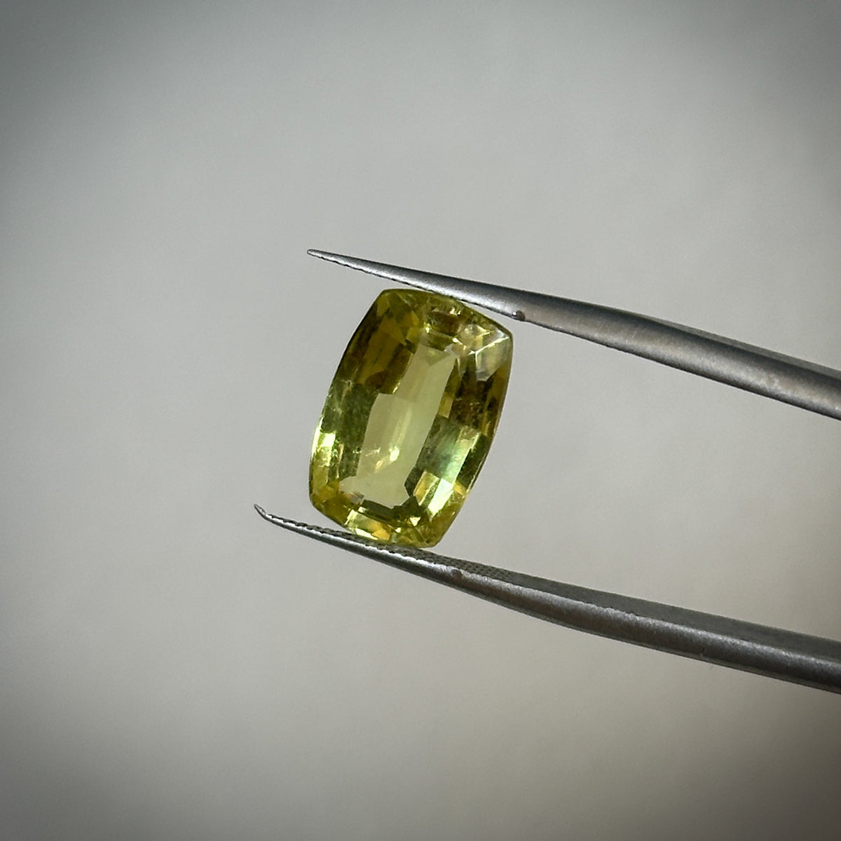 fancy cushion cut medium toned yellow-green chrysoberyl gemstone held in tweezers 
