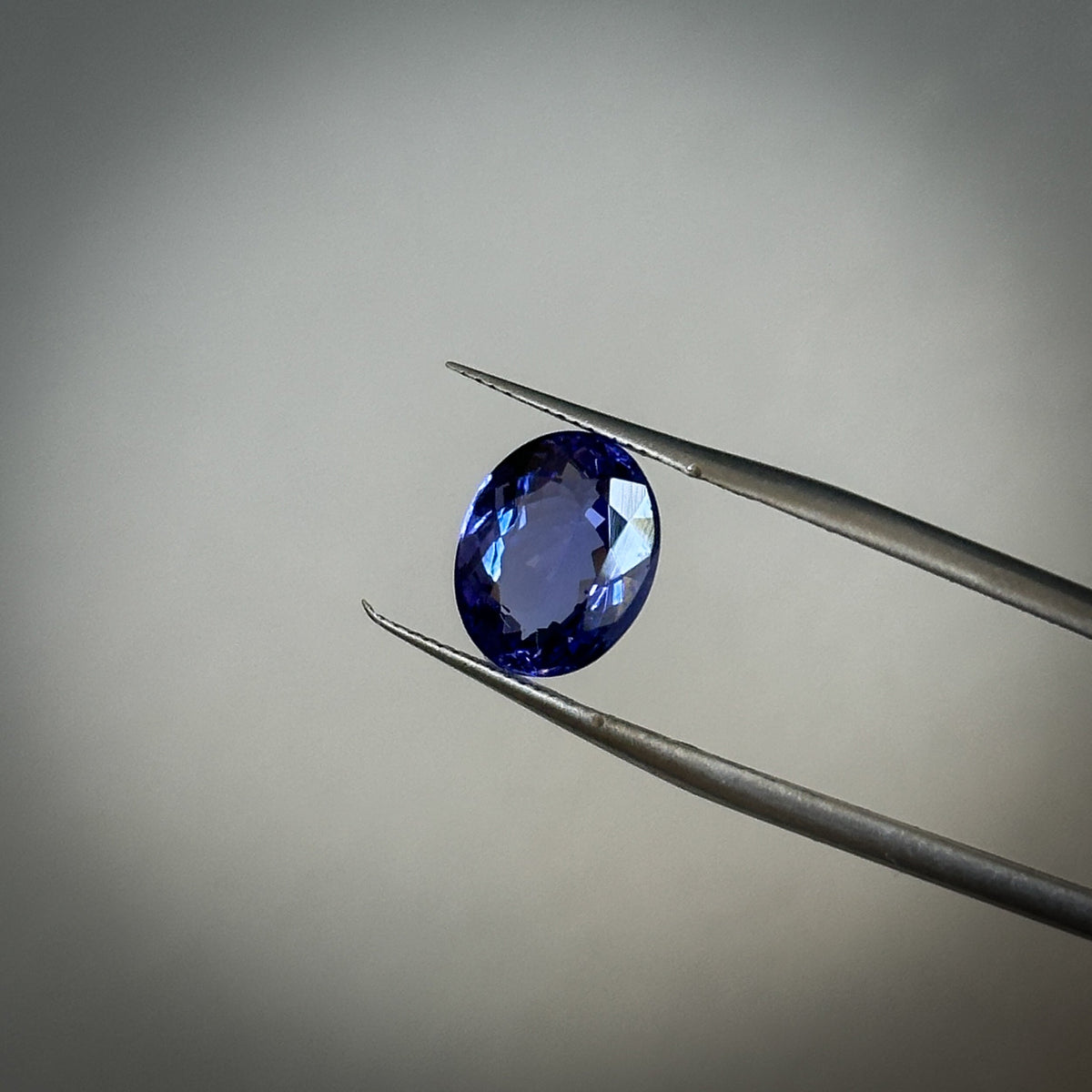 fancy oval cut deep toned blue-ish purple tanzanite gemstone held in tweezers 