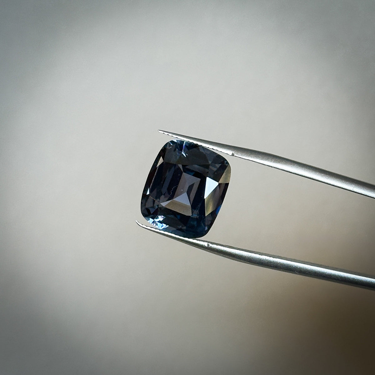 fancy cushion cut color change purple-ish blue spinel gemstone held in tweezers 